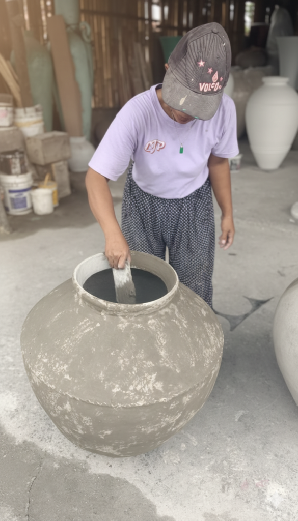 Artisane balinaise appliquant à la main la finition intérieure d’un grand vase en terre cuite, illustrant la fabrication artisanale traditionnelle.