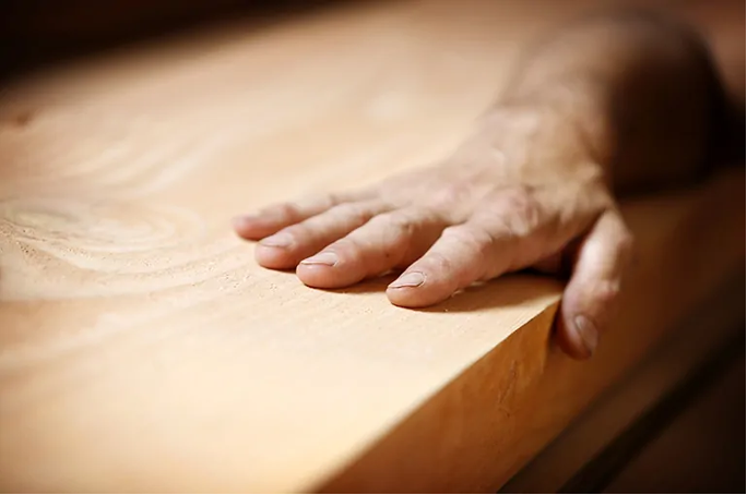 Main d’artisan caressant une surface en bois naturel lisse
