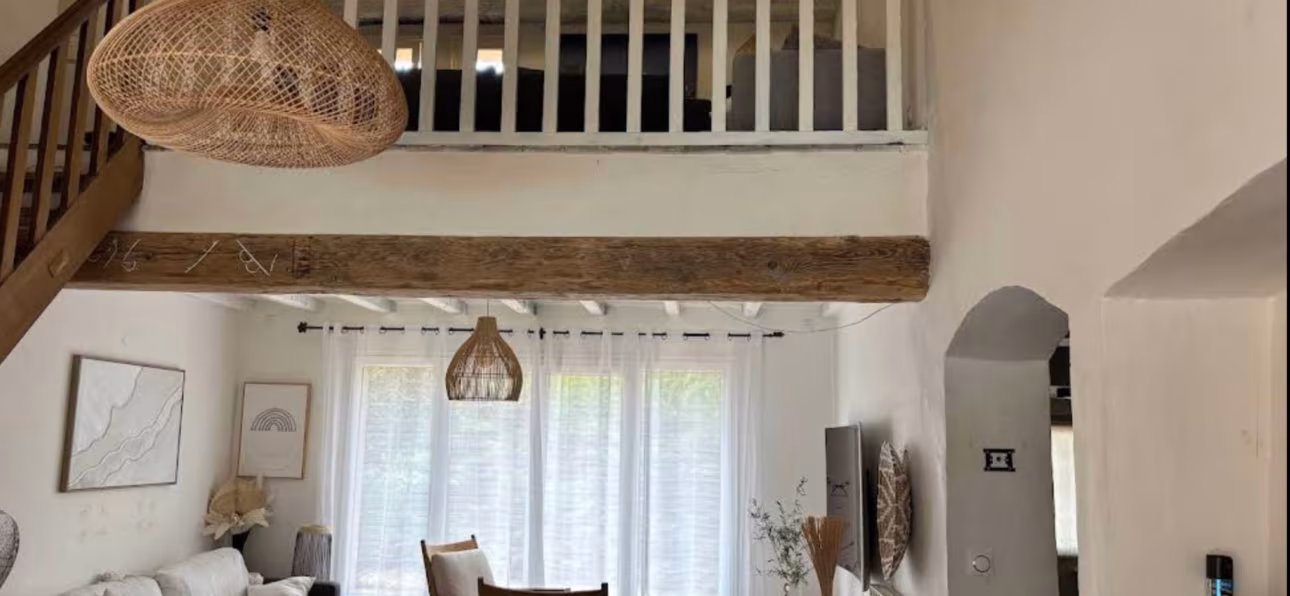 Salon bohème avec suspension en rotin, meubles en bois et décoration naturelle dans un intérieur lumineux.