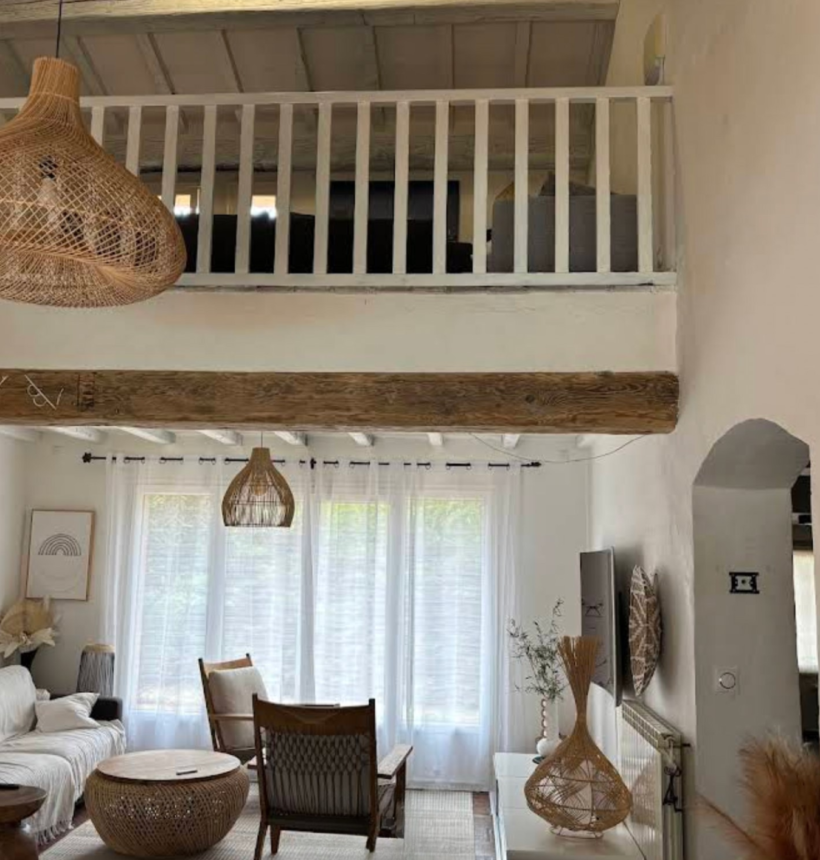 Salon bohème avec suspension en rotin, meubles en bois et décoration naturelle dans un intérieur lumineux.