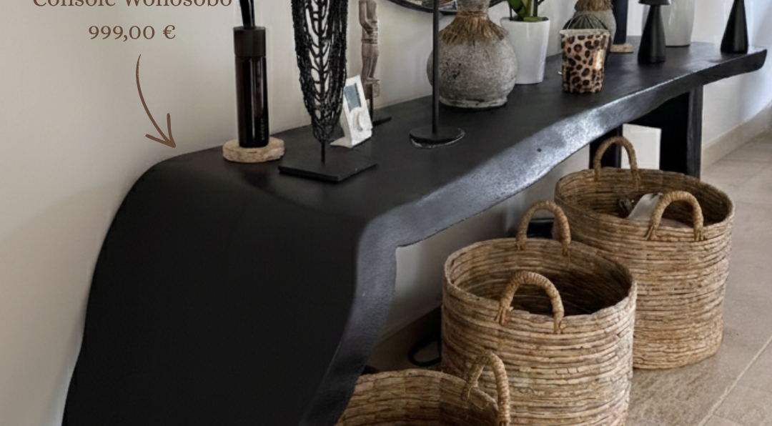Salon bohème chic avec console Wonosobo noire en bois décorée d’objets artisanaux, panier en fibres naturelles et miroir rond.