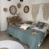 Chambre bohème adulte chaleureuse avec décoration murale en fibres naturelles, macramé et coussins aux tons verts et beiges, décoration bohème, esprit Quiet Luxury.
