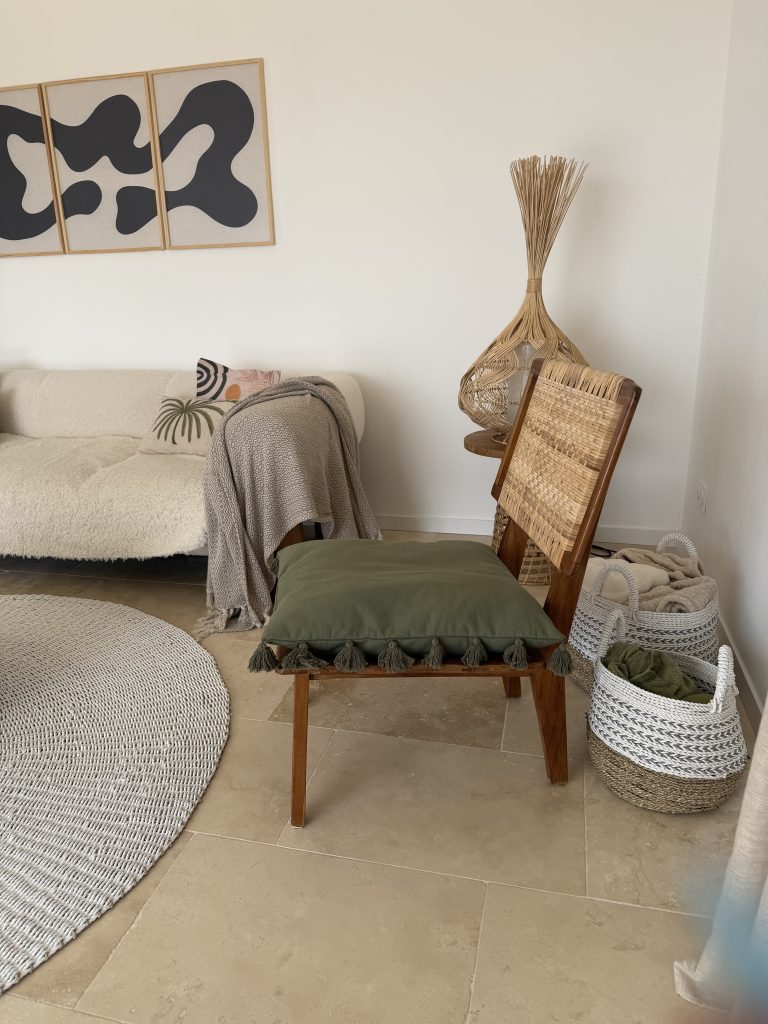 Salon bohème moderne avec fauteuil en bois et rotin, coussin vert à pompons et décoration naturelle épurée
