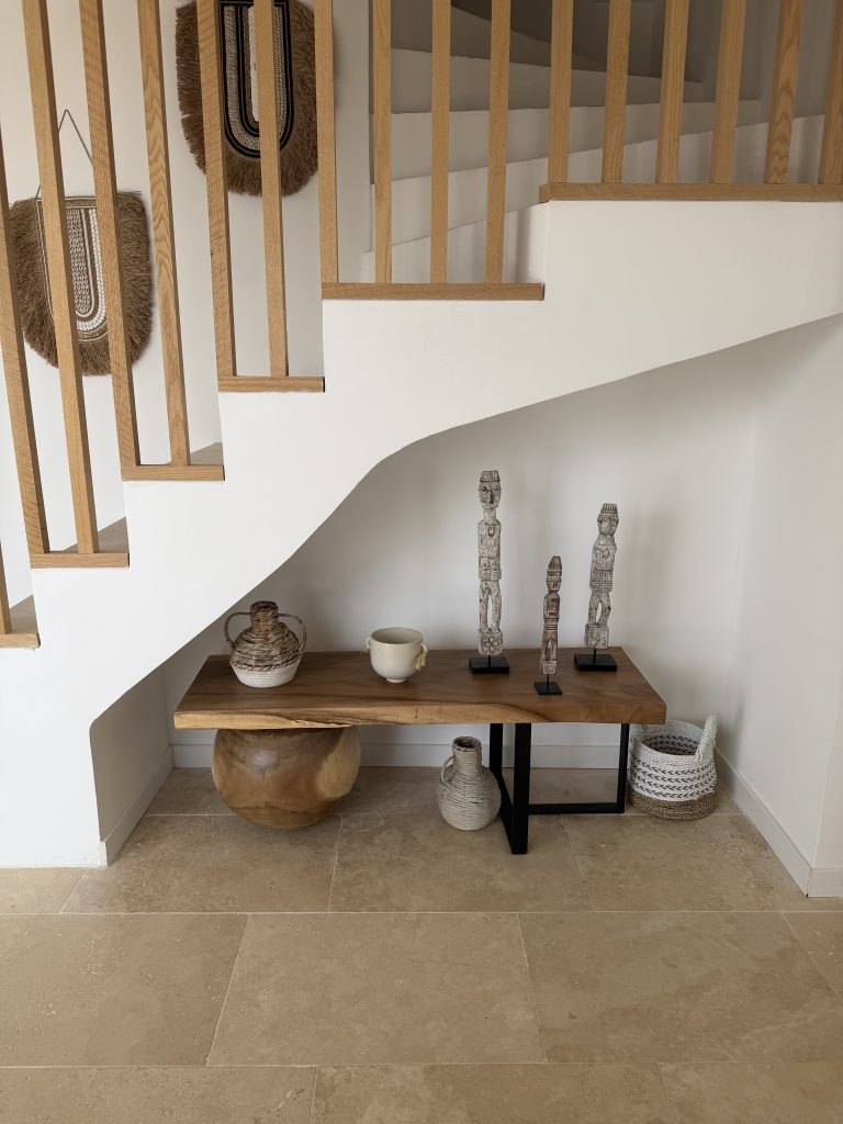 Aménager salon bohème avec console en bois naturel, objets artisanaux et décoration en fibres naturelles sous un escalier